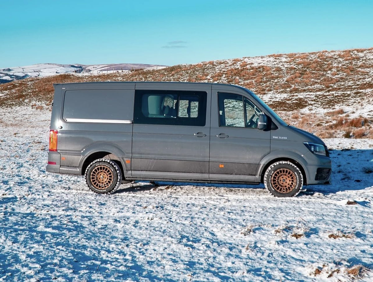 A grey MAN TGE on bronze Rogue wheels, side-on at wheel height, on a snowy moor