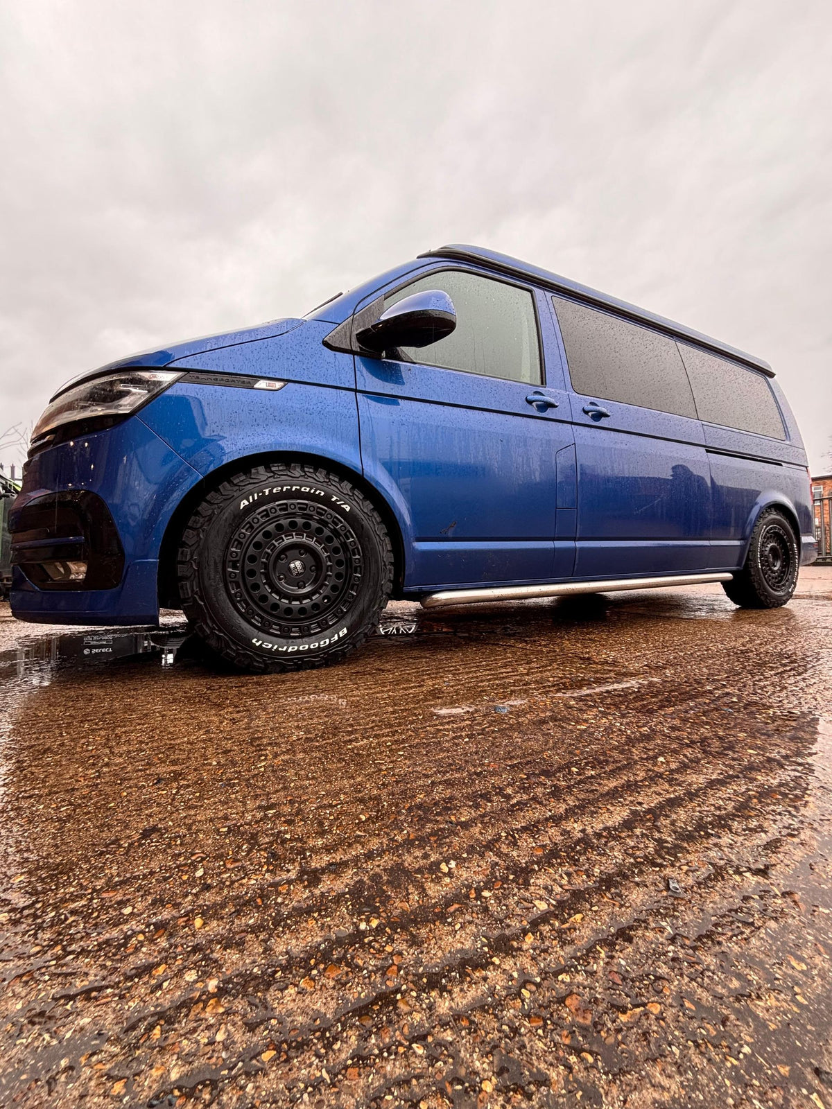 A blue Volkswagen Transporter on black Rogue wheels, parked on rippled sand