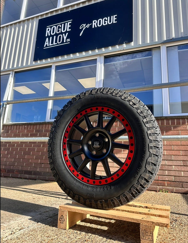 A black Rogue wheel with a red bead ring and all-terrain tyre on a pallet outside the Rogue workshop