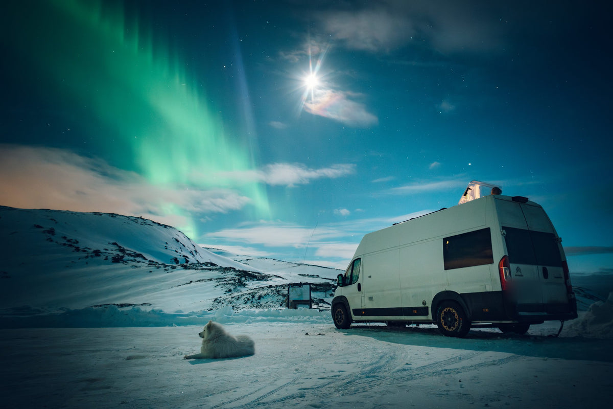 A white camper van under the northern lights on a snowy mountain plateau