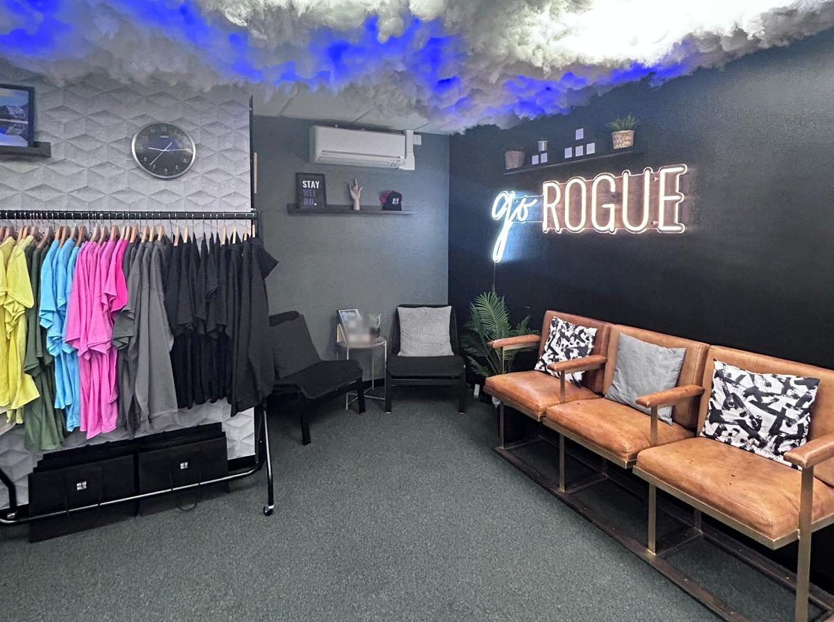 The Rogue showroom lounge: tan leather seats under the go ROGUE neon, the merch rail beside them
