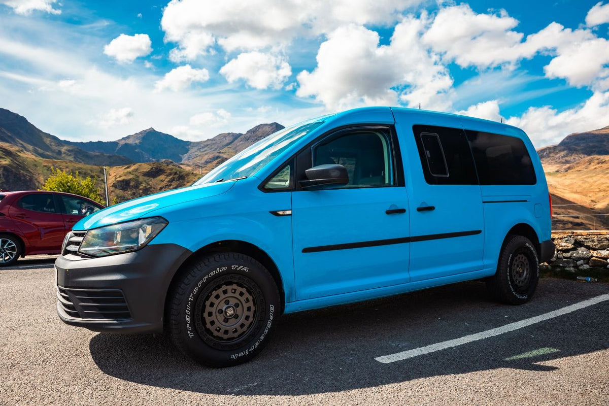 A bright blue Volkswagen Caddy on black Rogue wheels and BFGoodrich all-terrain tyres, mountains behind