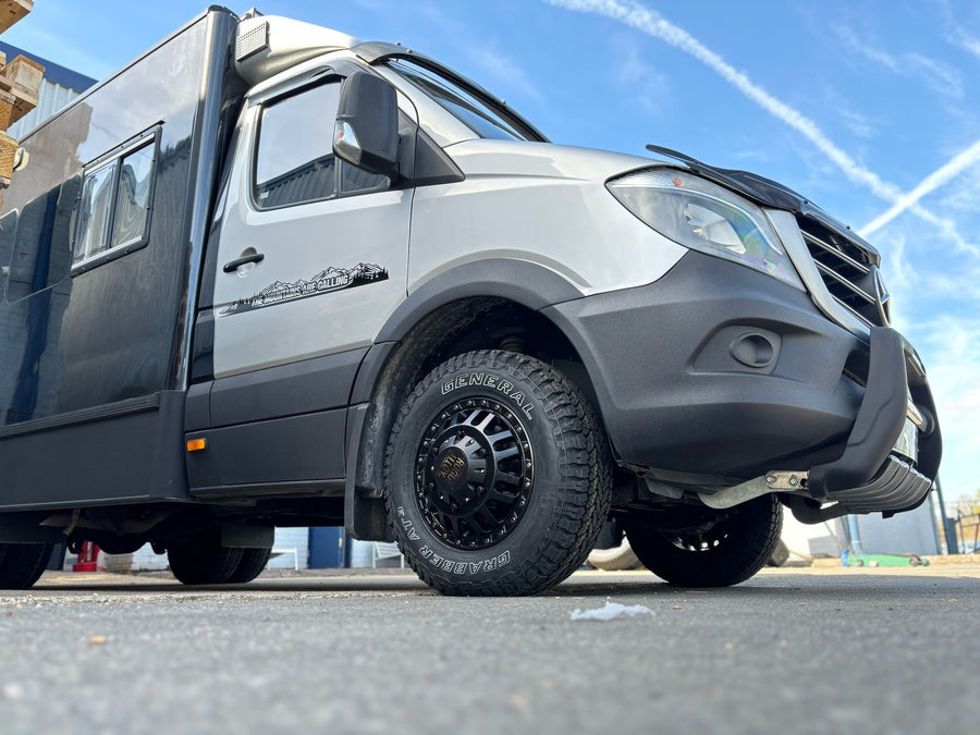 A Mercedes-Benz Sprinter 4x4 expedition conversion on black Rogue wheels, General Grabber AT3, in an industrial yard